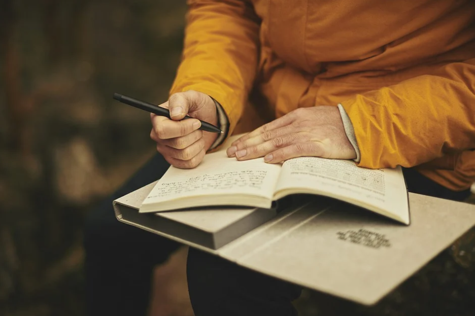 person in a yellow jacket writing on a journal